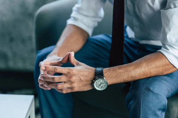 Cropped view of businessman sitting in armchair with folded hands — Stock Photo