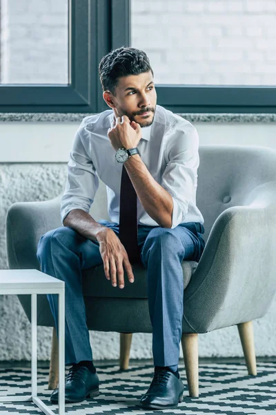 Hombre de negocios serio sentado en sillón y mirando hacia otro lado - foto de stock