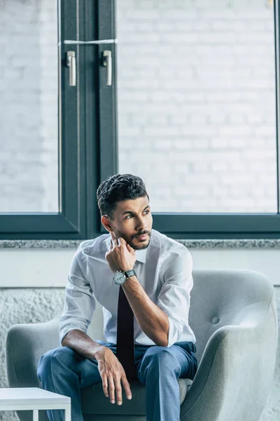 Serious businessman sitting in armchair near window and looking away — Stock Photo