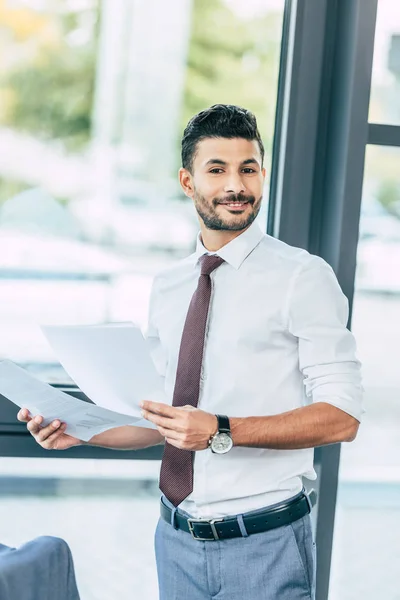 Handsome businessman holding documents, smiling and looking at camera — Stock Photo