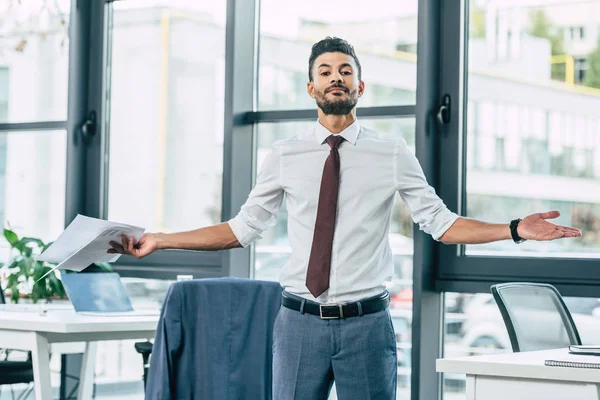 Junger Geschäftsmann zeigt leider Geste, während er Dokumente hält und in die Kamera schaut — Stockfoto