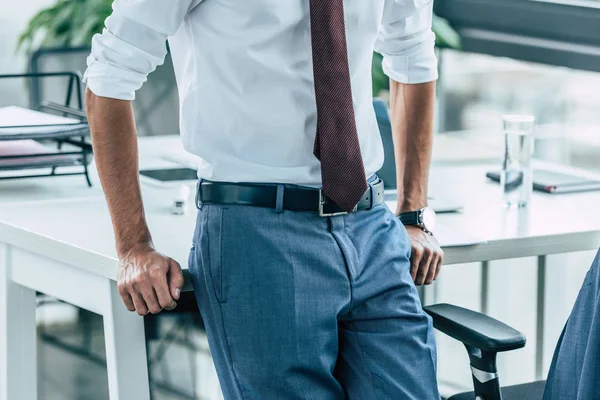 Обрезанный взгляд бизнесмена, стоящего рядом с рабочим местом в офисе — стоковое фото