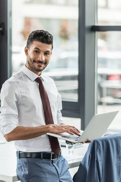Young businessman holding laptop and smiling at camera — Stock Photo