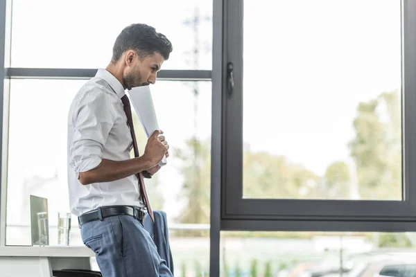 Thoughtful businessman holding documents while standing at workplace — Stock Photo