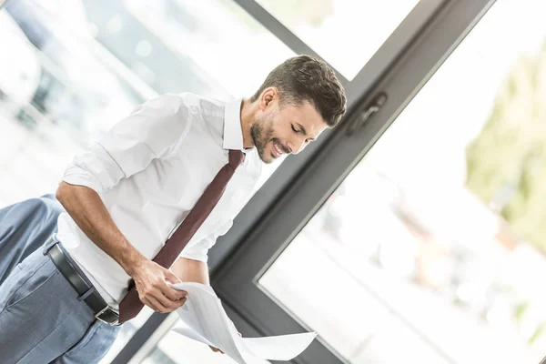Young businessman smiling while looking at papers in office — Stock Photo