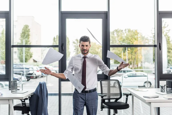 Uomo d'affari scontento gettando carte mentre in piedi in ufficio moderno — Foto stock