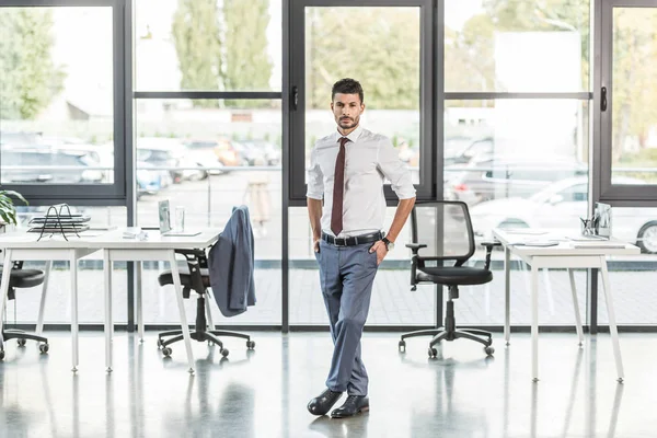 Jovem, homem de negócios confiante em pé no escritório moderno e olhando para a câmera — Fotografia de Stock