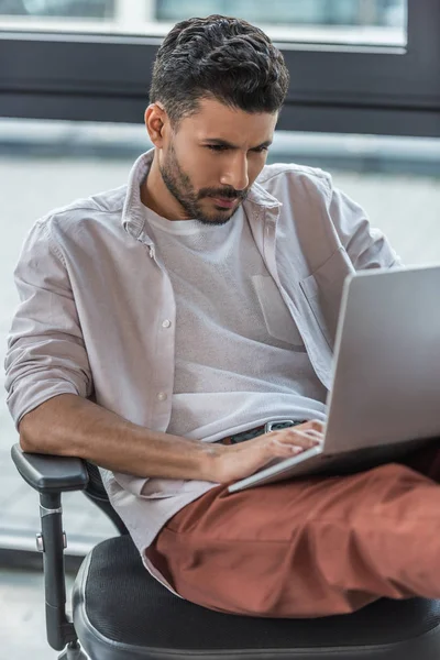 Homem de negócios concentrado sentado na cadeira de escritório e usando laptop — Fotografia de Stock