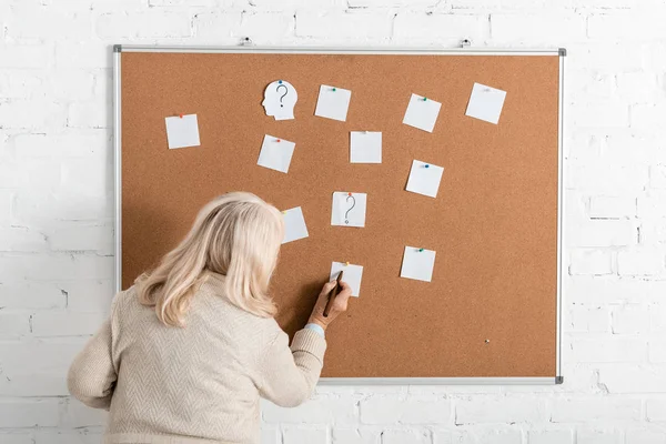Back view of retired woman with alzheimer disease writing on paper near board — Stock Photo