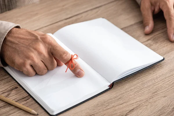 Cropped view of senior man with alzheimers disease string human finger reminder near notebook — Stock Photo