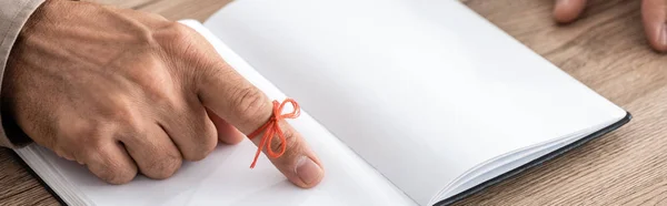 Panoramic shot of senior man with alzheimers disease string human finger reminder near notebook — Stock Photo