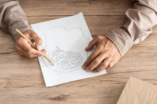 Vista recortada del hombre jubilado con enfermedad de Alzheimer dibujando la cabeza humana y el cerebro - foto de stock