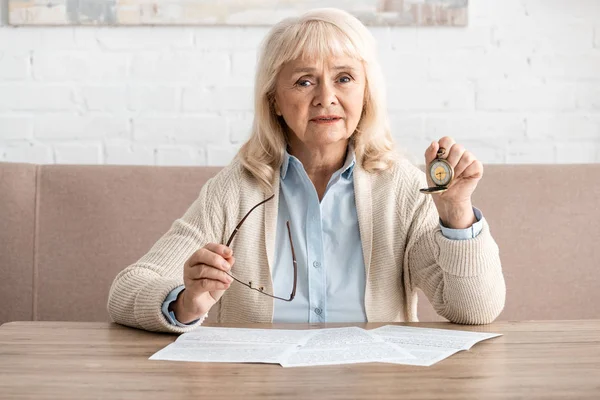 Femme retraitée tenant montre de poche et lunettes près des papiers sur la table — Photo de stock