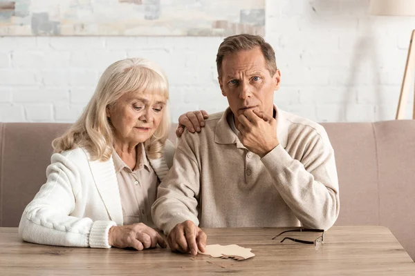 Hombre mayor en la enfermedad de Alzheimer sentado cerca de esposa triste - foto de stock