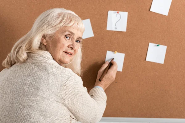 Расстроена старшая женщина с болезнью Альцгеймера держа маркер ручку возле бумаги на борту — стоковое фото