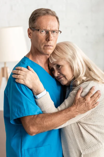 Molesto mujer mayor abrazando doctor en gafas - foto de stock