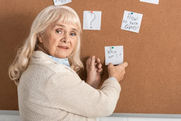Selective focus of senior woman with alzheimer disease touching paper with who am i letters — Stock Photo