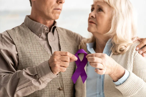 Vue recadrée d'un homme et d'une femme âgés tenant un ruban violet — Photo de stock