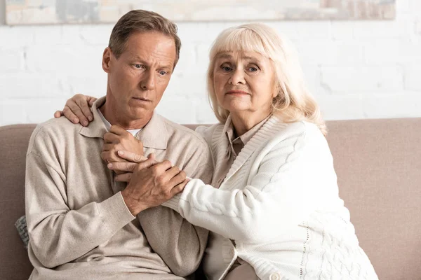 Грустная женщина на пенсии обнимает мужа с психическими расстройствами дома — стоковое фото