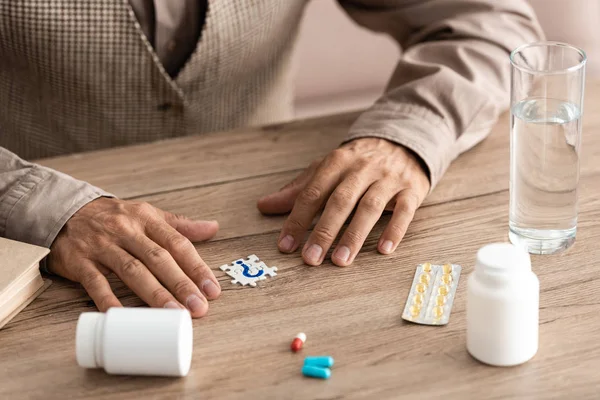 Cropped view of sick man sitting near jigsaw with question mark and bottles — Stock Photo