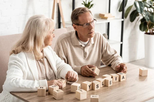 Seniorin schaut kranken Mann in der Nähe von Holzwürfeln mit Legasthenie-Buchstaben an — Stockfoto