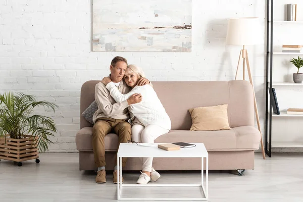 Senior husband hugging sick wife with mental illness while sitting on sofa at home — Stock Photo