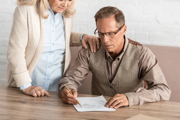 Ausgeschnittene Ansicht einer Seniorin, die neben Ehemann mit psychischer Erkrankung steht, Zeichnung auf Papier — Stockfoto