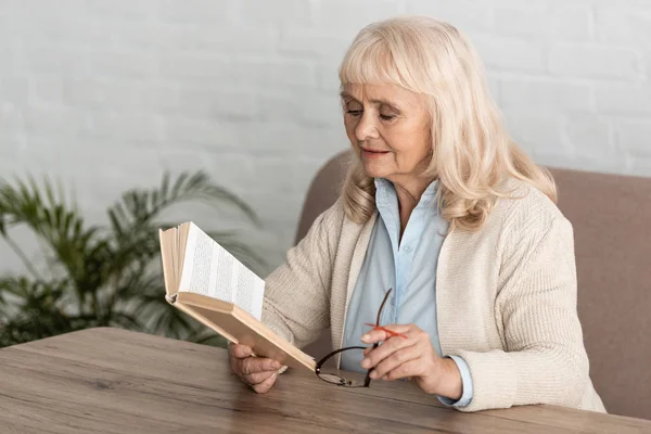 Senior woman with alzheimers disease string human finger reminder reading book and holding glasses — Stock Photo