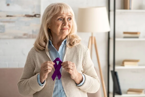 Triste jubilada sosteniendo púrpura cinta en casa - foto de stock