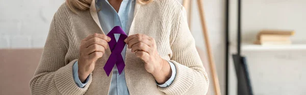 Plano panorámico de la mujer jubilada sosteniendo cinta púrpura en casa - foto de stock