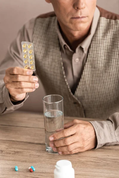 Vista recortada del hombre jubilado con la enfermedad de Alzheimer que contiene pastillas y un vaso de agua - foto de stock