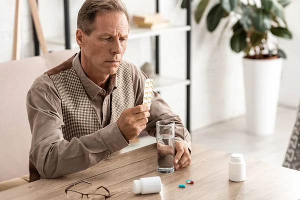Foco seletivo do homem aposentado com pílulas de retenção de doença de alzheimer e vidro de água — Fotografia de Stock