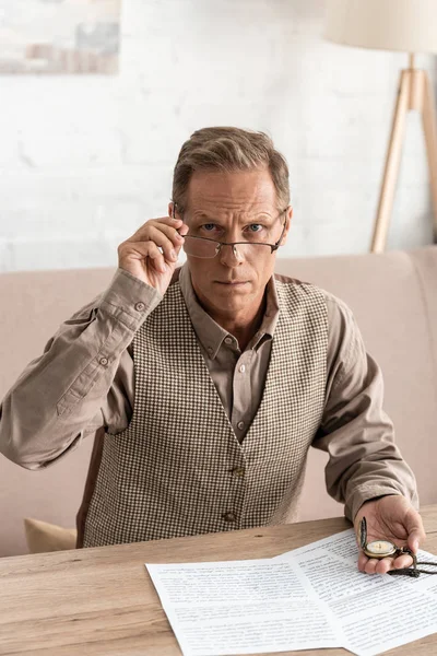 Senior man in glasses holding pocket watch near papers with letters — Stock Photo