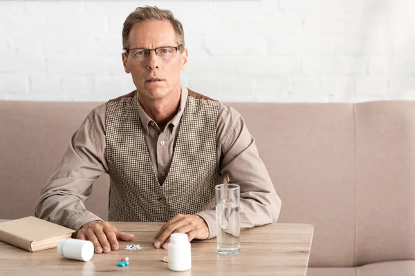 Retired man with mental illness sitting near pills on table — Stock Photo