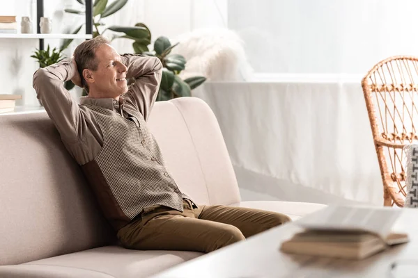 Selective focus of cheerful senior man sitting on sofa and gesturing at home — Stock Photo