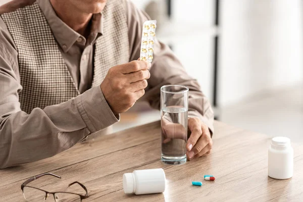 Vista recortada de un hombre jubilado con enfermedad mental sosteniendo pastillas - foto de stock