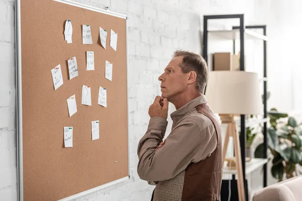 Pensive retired man with alzheimer looking at board with papers — Stock Photo