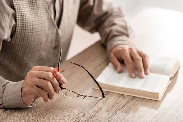 Обрезанный вид пенсионера с болезнью Альцгеймера струны человеческого пальца напоминание держа очки возле книги — стоковое фото