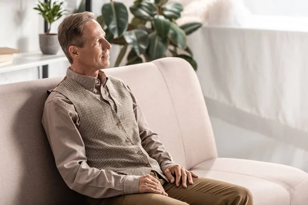 Веселый пенсионер сидит дома на диване — стоковое фото
