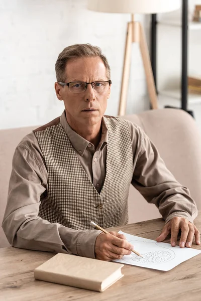 Senior man with mental illness drawing on paper near book — Stock Photo