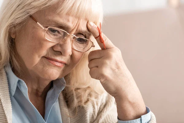Pensive senior woman with alzheimers disease string human finger reminder — Stock Photo