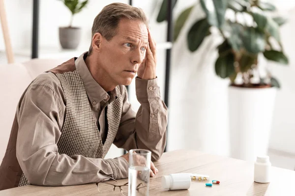 Sick retired man with memory loss sitting near pills and bottles on table — Stock Photo