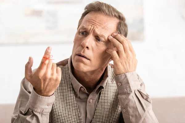 Selective focus of confused retired man looking at alzheimers disease string human finger reminder — Stock Photo