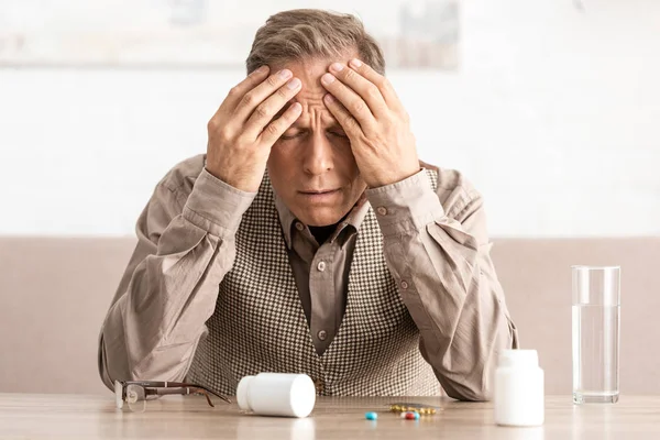 Enfermo jubilado con enfermedad de Alzheimer cerca de pastillas y frascos en la mesa - foto de stock