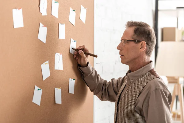 Side view of retired man with alzheimer illness holding pencil near board with papers — Stock Photo