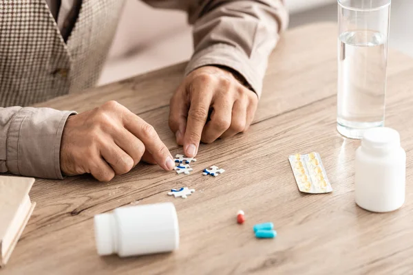 Vista recortada del hombre retirado juego de piezas del rompecabezas en la mesa - foto de stock