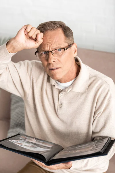 Disgustada hombre mayor en gafas celebración álbum de fotos - foto de stock