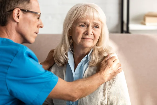 Selective focus of doctor in glasses touching upset senior woman — Stock Photo