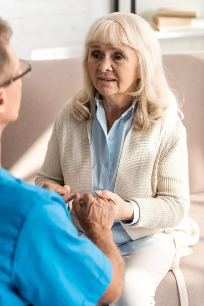 Selective focus of doctor holding hands with sick retired woman — Stock Photo