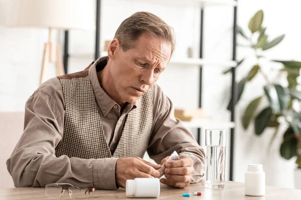 Upset senior man with alzheimer disease holding pills — Stock Photo